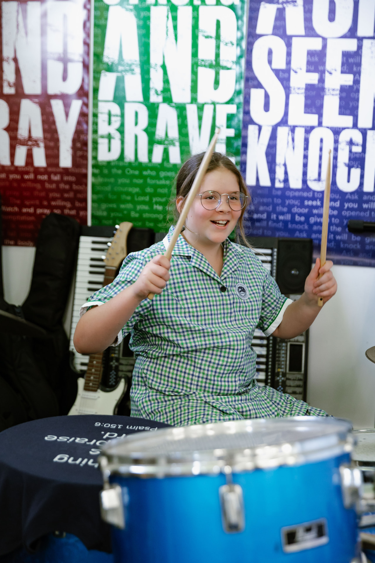 A Border Rivers student smiling while playing the drum kit in the College music room